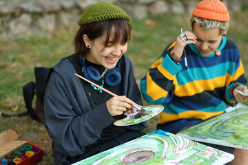 two young and innovative female artists conducting an outdoor painting lesson. Surrounded by...