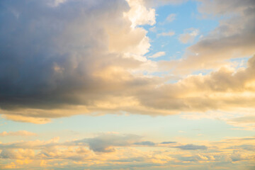The sky is adorned with soft, fluffy clouds illuminated by warm golden light as day transitions into night, creating a peaceful atmosphere in the horizon.