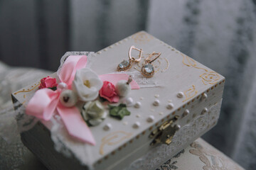 A box with a pink ribbon and a pair of earrings inside. The earrings are gold and blue