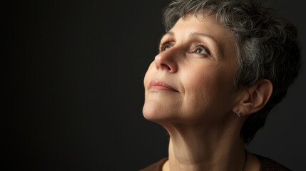 A serene studio portrait of a mature woman looking up, with natural light illuminating her face