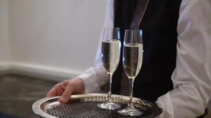A waiter in formal attire is elegantly serving four glasses of champagne on a silver tray at a sophisticated event. Hands are seen reaching for the drinks in this glamorous setting - Powered by Adobe