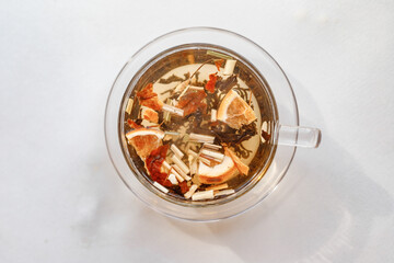 Pouring boiling water from kettle in a glass cup for brewing tea in the kitchen on white table, white background, top view
