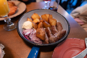 Flavorful grilled meat paired with roasted potatoes, sliced onions, served in rustic pan at restaurant.