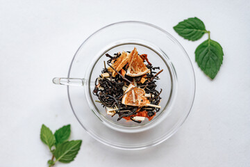 Dried tea leaves in glass cup on white background top view 