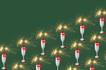 Champagne glass full of christmas decoration, red bow with sparkler on green background. Happy holiday celebration event pattern with copy space.