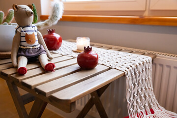 handmade soft doll, decorative garnet form ceramics, lit candle sits on macrame woven runner on wooden table. cozy indoor