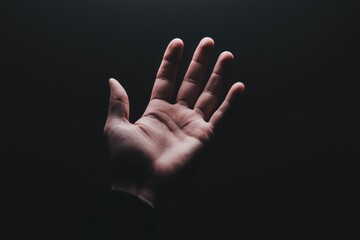 Dramatic close-up of a hand reaching into pitch-black space, light and shadows capturing tension, mystery, and human connection