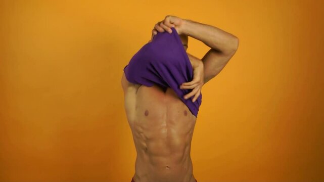 Summer mood. Young athletic man posing in studio on orange background.