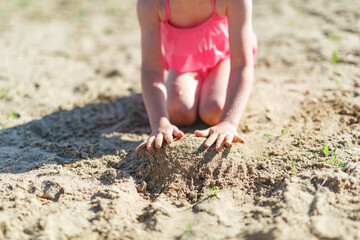 Girl playing on a sandy beach on summer vacation. A child is building a sand castle on the sea.