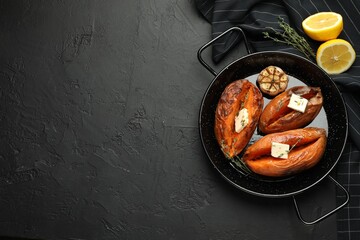 Tasty cooked sweet potatoes with feta cheese, garlic, thyme and lemon on black table, top view. Space for text