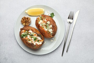 Tasty baked sweet potatoes with feta cheese, parsley, garlic and lemon slice on light textured table, top view