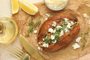 Tasty baked sweet potato with feta cheese, lemon and herbs on light textured table, flat lay