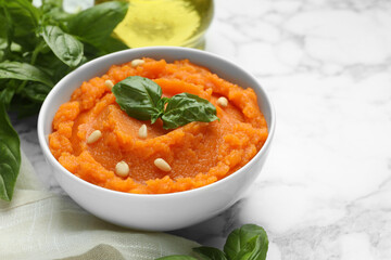 Tasty mashed sweet potato with basil and seeds in bowl on white marble table, closeup