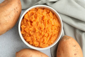 Tasty mashed sweet potato in bowl and fresh vegetables on gray table, flat lay