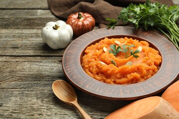Tasty mashed sweet potato with pumpkin seeds in bowl, spoon, parsley and spices on wooden table, closeup