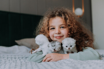 little girl with curly hair hugs little kittens at home