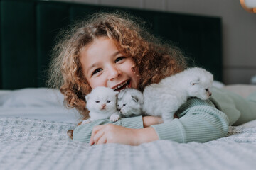 little girl with curly hair hugs little kittens at home