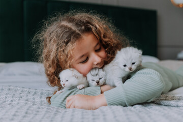 little girl with curly hair hugs little kittens at home