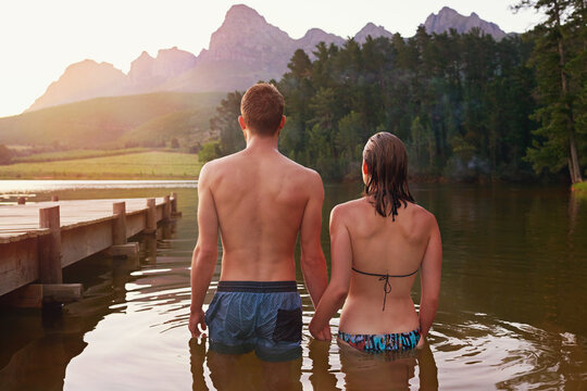 Swimming, sunset and back of couple at lake together on vacation, romantic anniversary or holiday. Relationship, support and people in water for bonding, love or trust on honeymoon date for travel