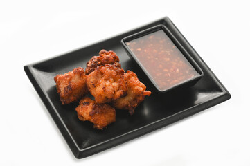 Crispy fried chicken with sauce in black tray on white background.