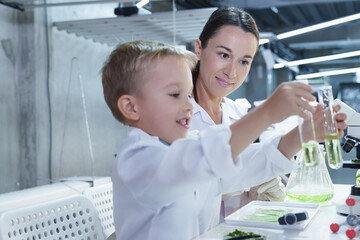 Happy mother and curious child mixing green liquids in test tubes during a science experiment,...