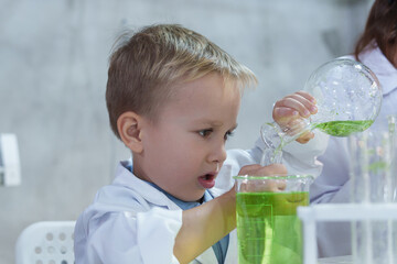 Happy mother and curious child mixing green liquids in test tubes during a science experiment,...