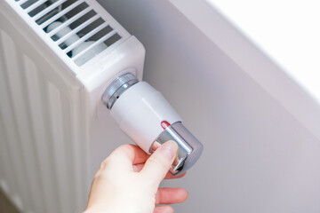Hand adjusting radiator valve to control room heating temperature