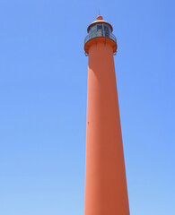 Orange lighthouse in minimalist style against bright blue sky.