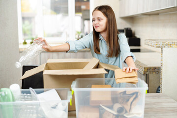 Child girl sorts paper and plastic into sorting bin in the kitchen at home. Sorting recycling items for plastic, paper and metal drop offs. Garbage separation concept.