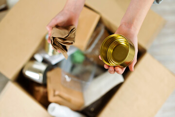 Kids hands sort paper and plastic into carton box at home. Top view. Waste segregation, waste sorting, waste recycle.