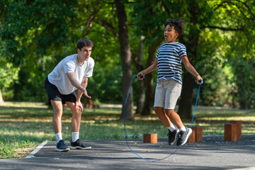 Trainer guides a child in an outdoor jump rope exercise session, focusing on improving coordination, agility, and overall fitness through fun and dynamic physical activity.