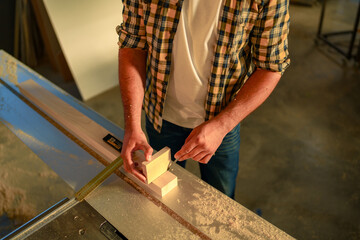 Close up on hands of carpenter who is draw on a piece of wood using a peace of other wood for precision.