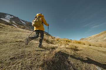 A tourist walks over rough terrain in trekking boots and bright clothes. A traveler with sticks in his hands. A man in bright clothes in the mountains.