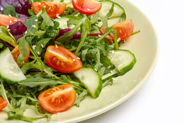 Vegetable salad of tomato, cucumber, greens with sesame on the plate.