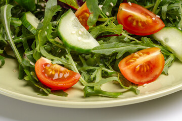 Vegetable salad of tomato, cucumber, greens with sesame on the plate.