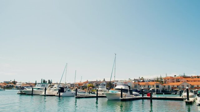 A vibrant marina scene features several boats moored at the docks, with charming buildings lining the waterfront under a bright, sunny sky.