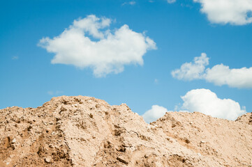 a mountain of sand against a blue sky and clouds