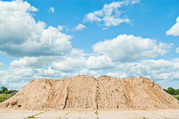 a mountain of sand against a blue sky and clouds