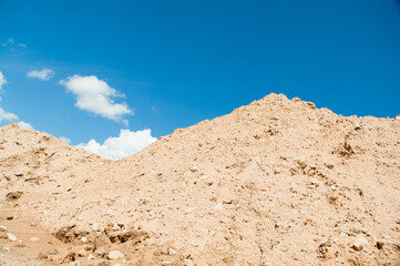a mountain of sand against a blue sky and clouds