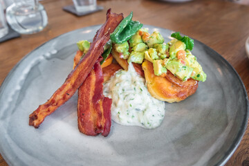 A tasty plate featuring sweet potatoes, bacon strips, and a creamy sauce, garnished with fresh greens and herbs.