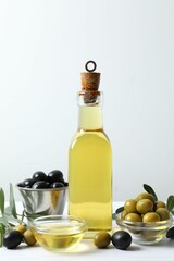 Bottle of fresh olive oil and olives with leaves on white background