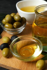 Bowl of fresh olive oil and olives with leaves on wooden background