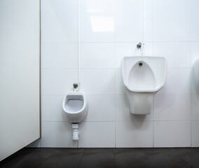 A pair of white porcelain urinals in a public interior space with white walls and black floor. One is for adults and another for children. Concept of big and small or high and low