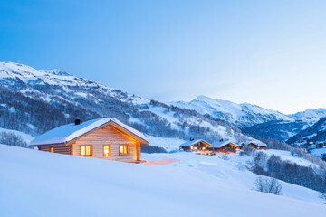 Fototapeta premium Snow-covered mountain cabin with warm Christmas lights aglow