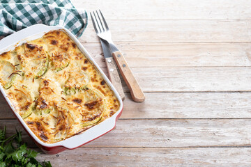 Casserole with cheese and gratin zucchini on wooden table. Copy space