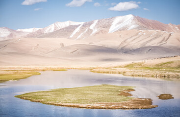 High mountain landscape panorama, a river in the mountains flows in a mountain valley among green meadows against the backdrop of mountains, landscape in the Pamir Mountains for background