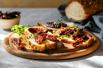 Slices of multigrain bread topped with sun-dried tomatoes and fresh thyme on a wooden board