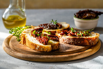 Slices of multigrain bread topped with sun-dried tomatoes and fresh thyme on a wooden serving board, bottle of olive oil in the background under warm natural light