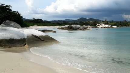 Tranquil beach with white sand, clear blue water, and large rocks.
