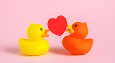 Two rubber ducks with red heart on pink background.